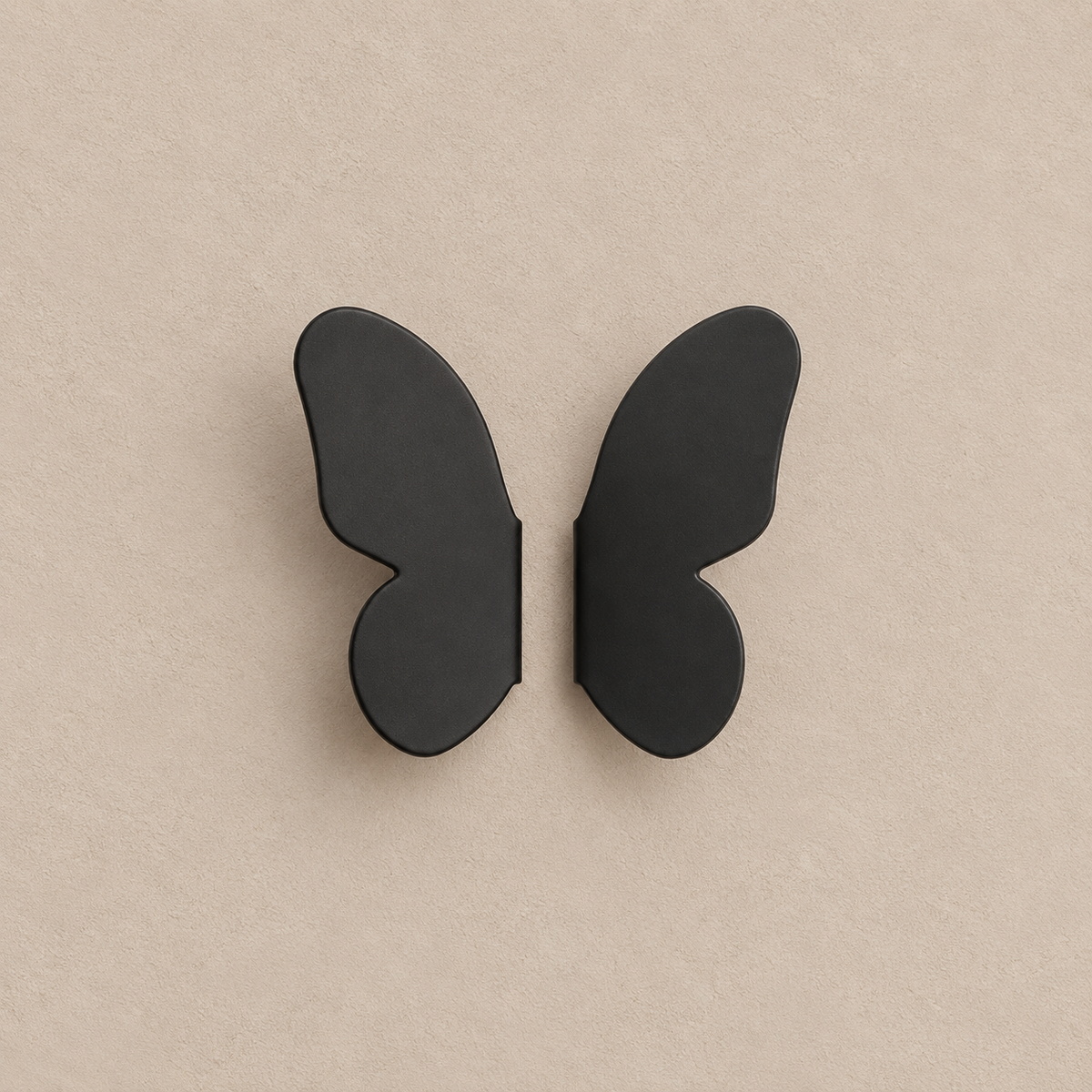 pair of matte black butterfly-wing cabinet knobs, two separate mirrored wings on a warm taupe background