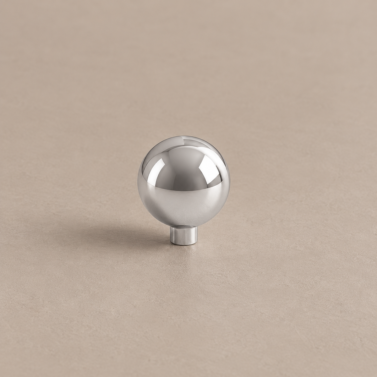 Polished chrome spherical cabinet knob with cylindrical stem on warm taupe surface