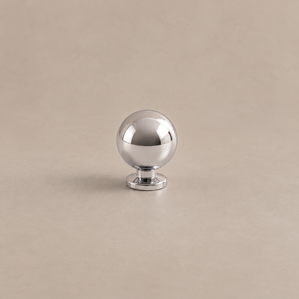 Polished chrome spherical cabinet knob with circular pedestal on warm taupe surface