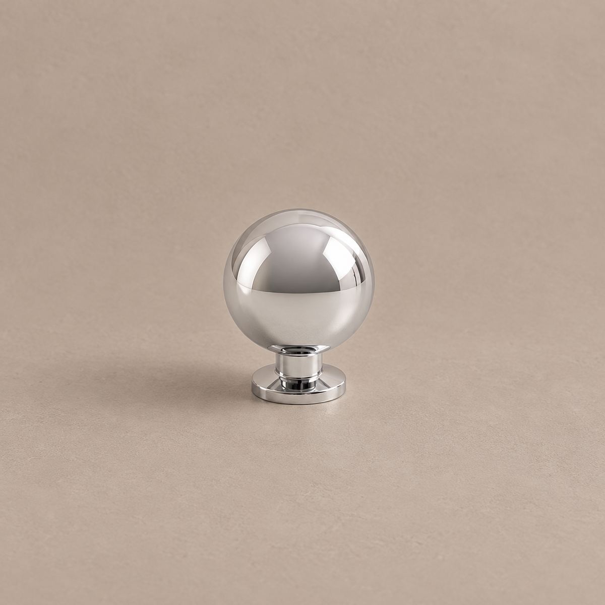Polished chrome spherical cabinet knob with circular pedestal on warm taupe surface