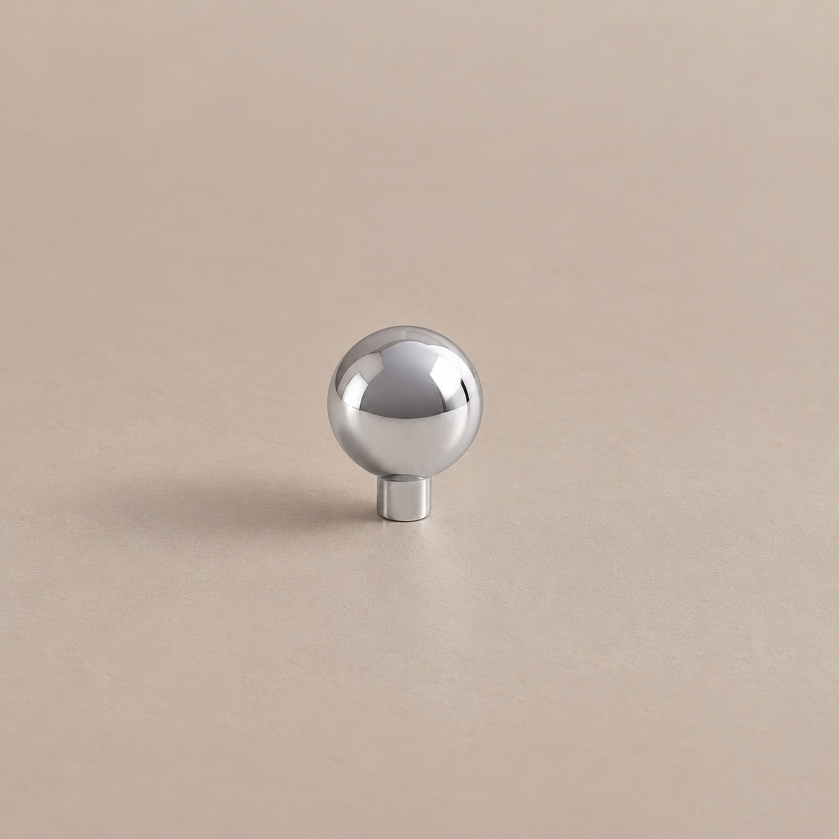 Polished chrome spherical cabinet knob with cylindrical stem on warm taupe surface