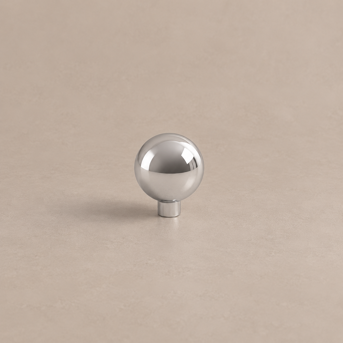 Polished chrome spherical cabinet knob with cylindrical stem on warm taupe surface
