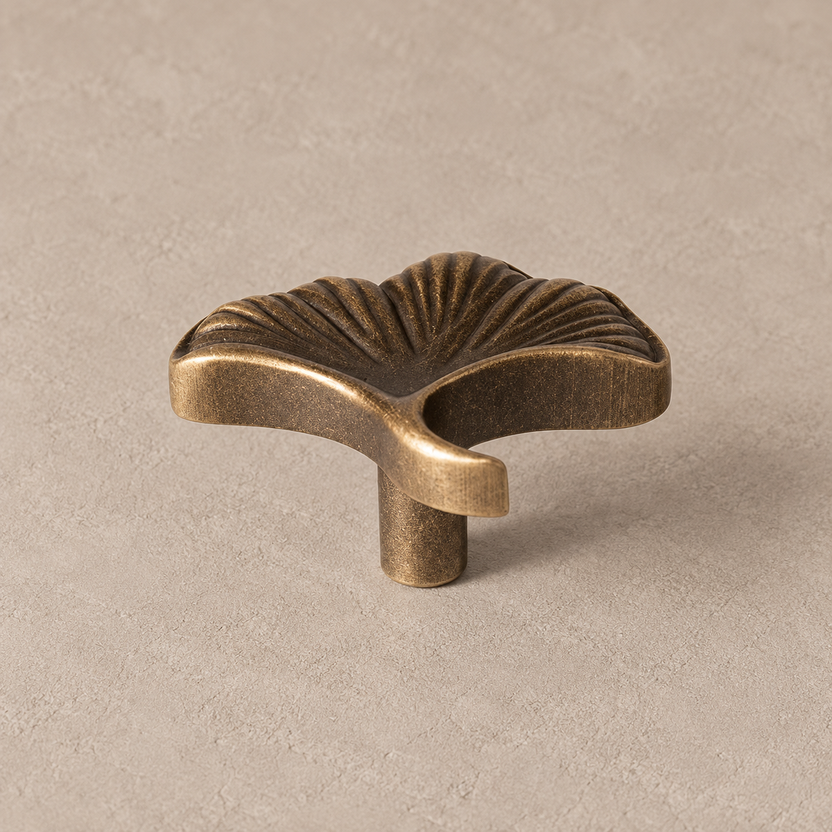 antique brass ginkgo leaf cabinet knob with fan-shaped deeply veined leaf, short curved stem and narrow mounting post on taupe studio surface