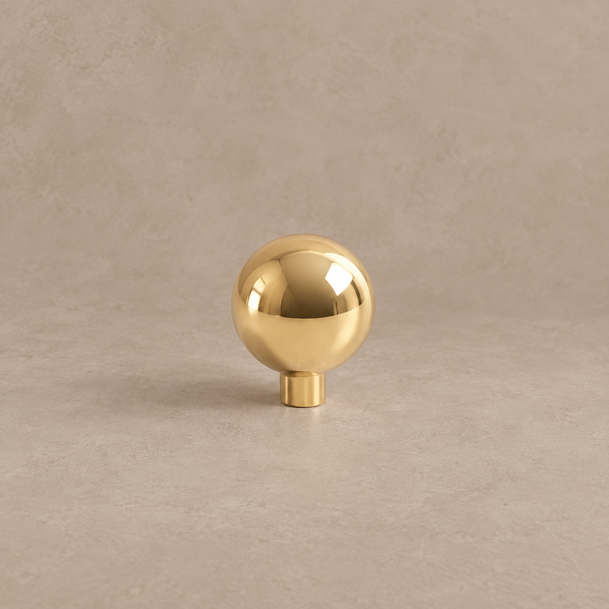 Polished brass ball cabinet knob on a taupe studio background
