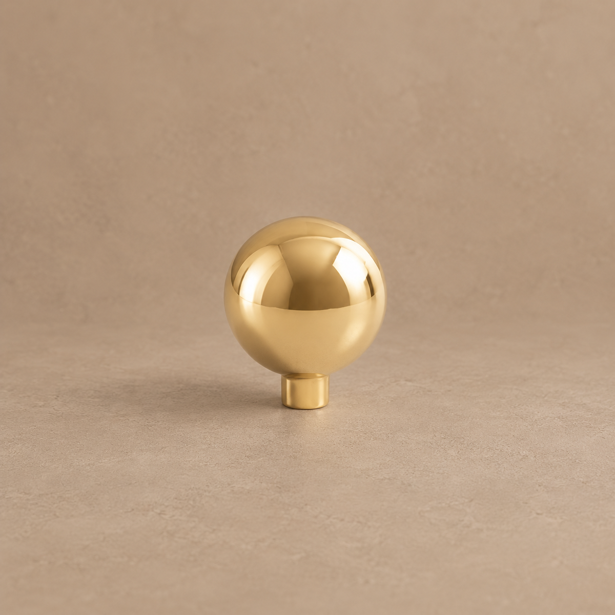 Polished brass ball cabinet knob on a taupe studio background