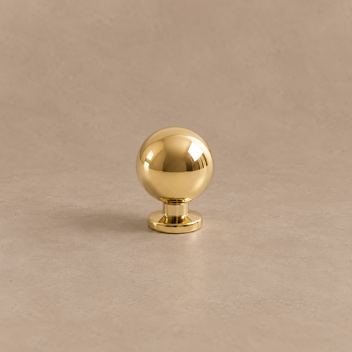 Polished brass ball cabinet knob on a taupe studio background