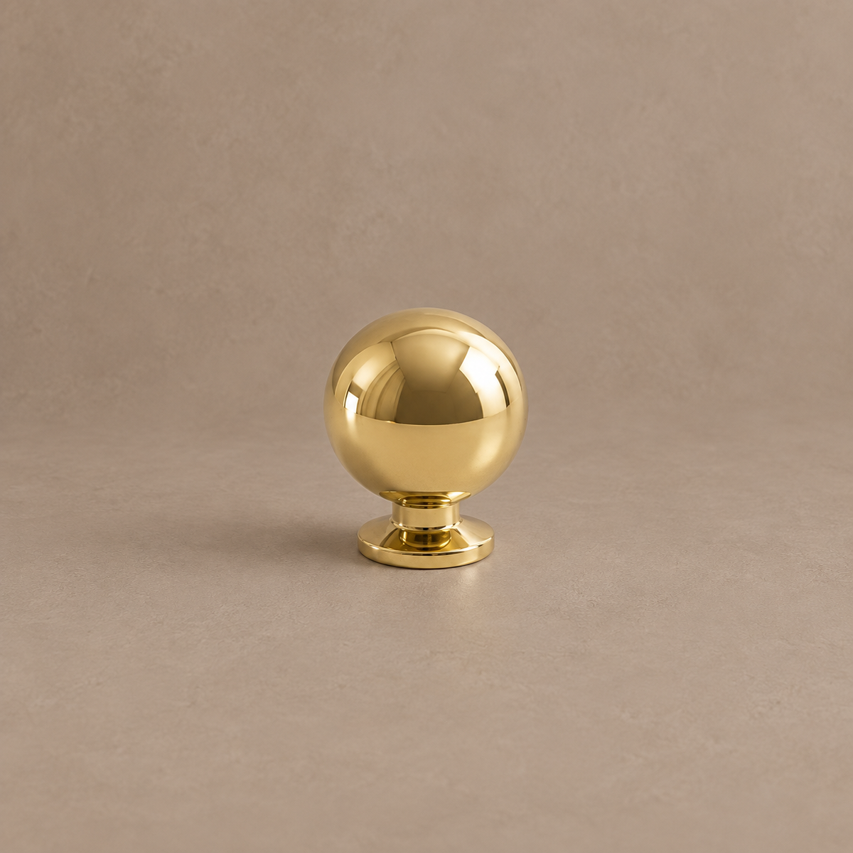 Polished brass ball cabinet knob on a taupe studio background