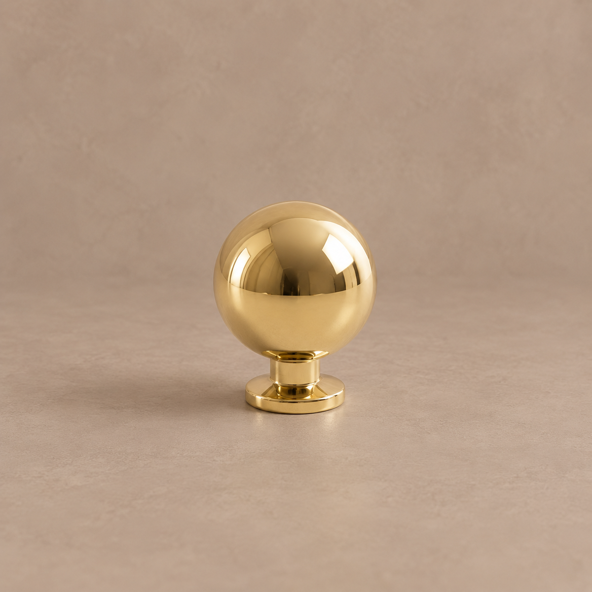 Polished brass ball cabinet knob on a taupe studio background