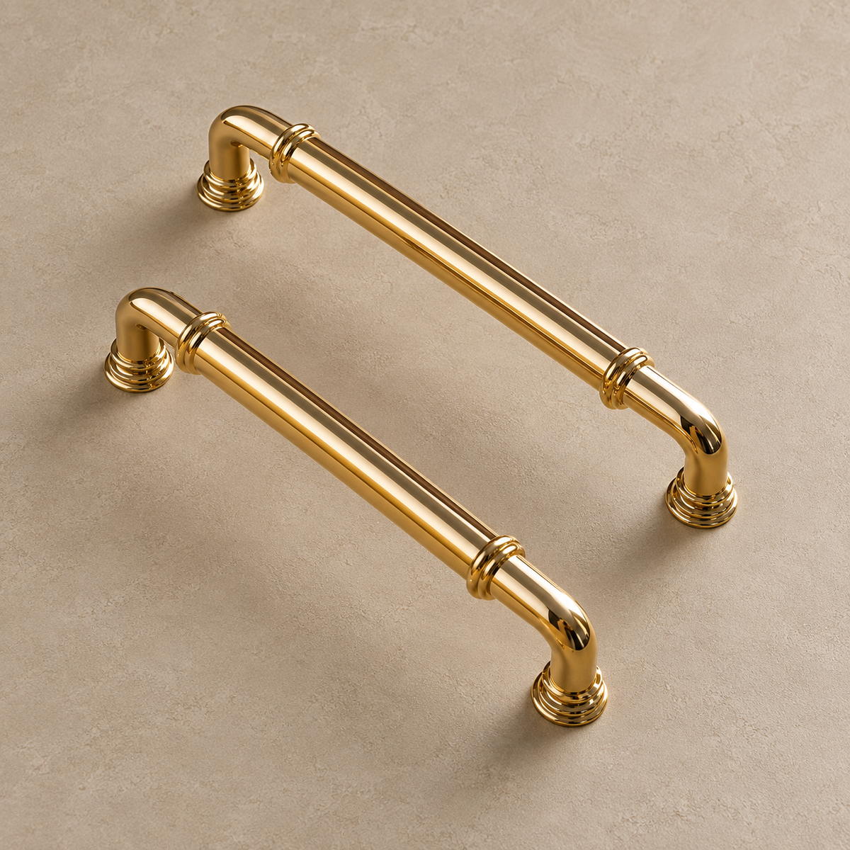 Polished brass cabinet pulls with curved elbows and ring collars on a taupe studio surface
