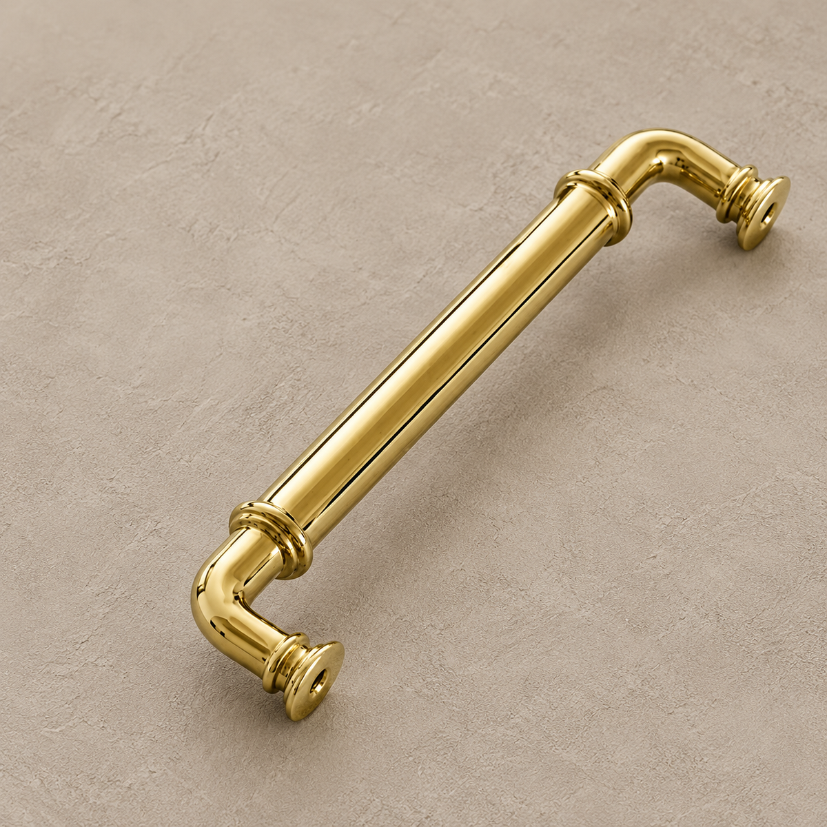 Polished brass cabinet pull with ringed collars on warm taupe plaster