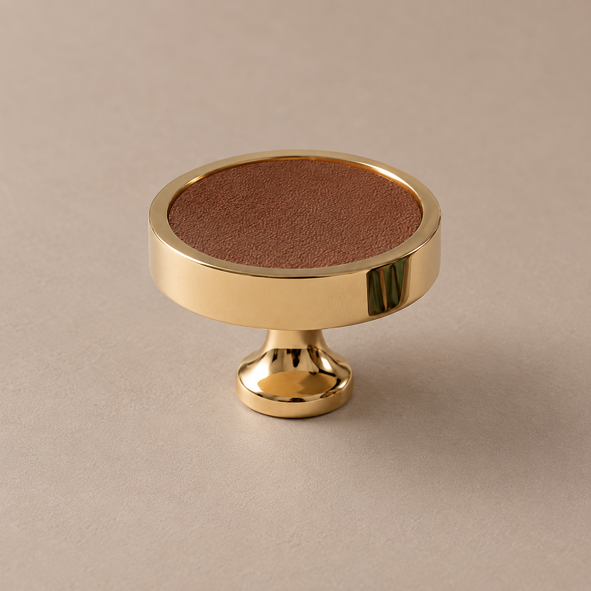 Polished PVD brass cabinet knob with brown cowhide leather inlay on taupe studio background