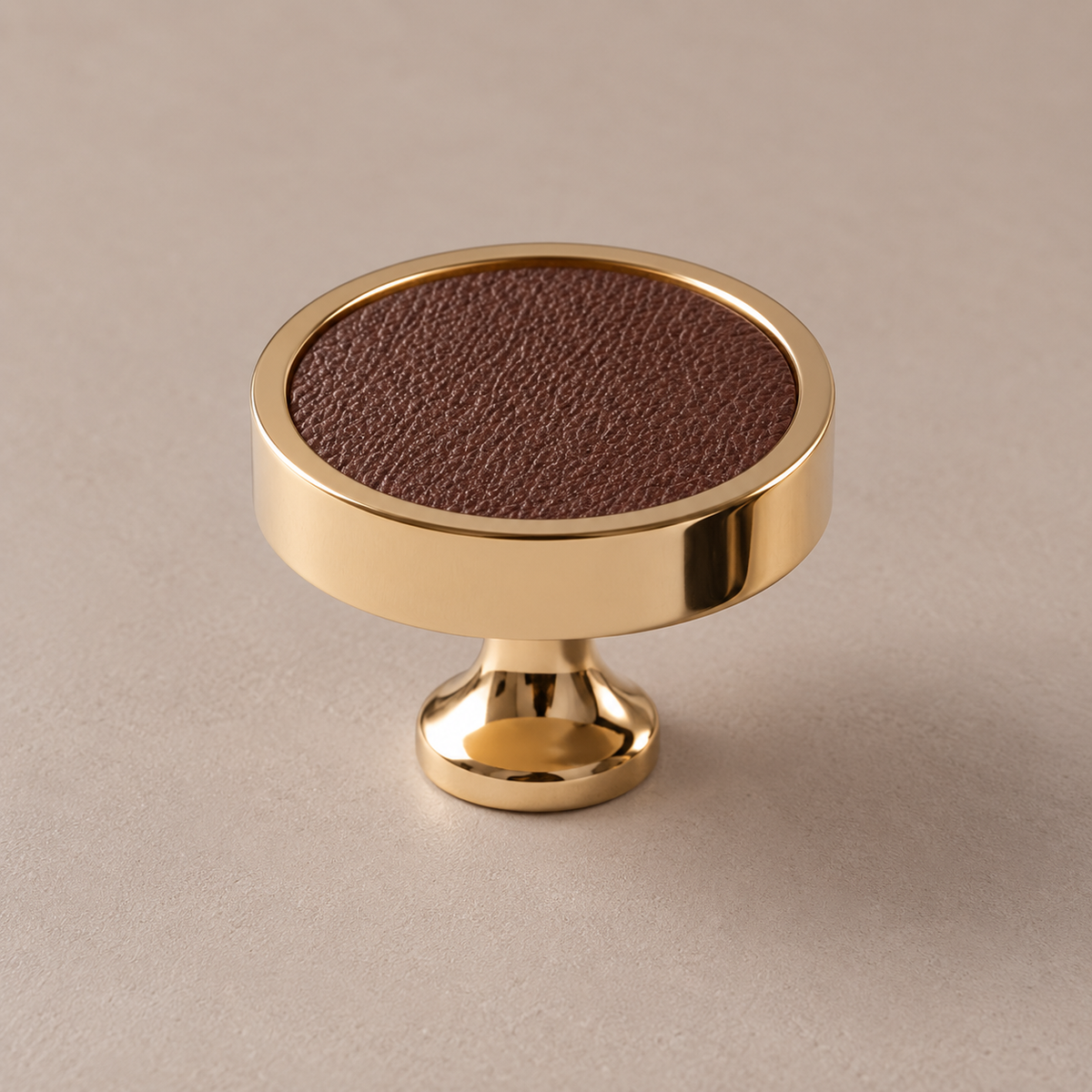Polished PVD brass cabinet knob with coffee cowhide leather inlay on taupe studio background