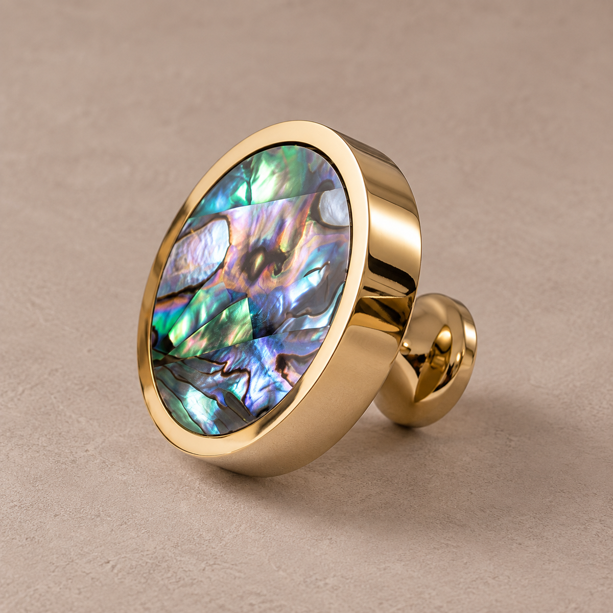 Polished PVD brass cabinet knob with green abalone shell inlay on taupe studio background
