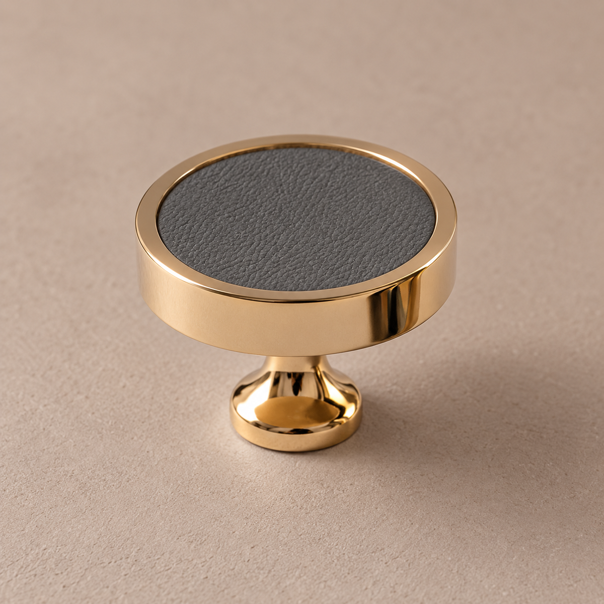 Polished PVD brass cabinet knob with grey cowhide leather inlay on taupe studio background