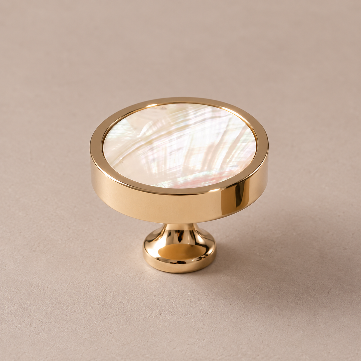 Polished PVD brass cabinet knob with white inlay on taupe studio background